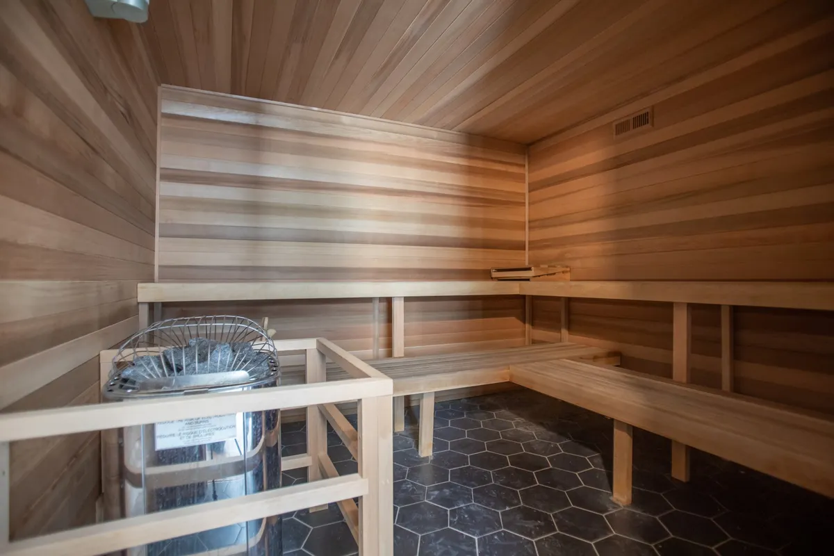 The interior features a soothing sauna environment with wooden benches and a metal stove, complemented by a hexagonal tiled floor. The space conveys tranquility and wellness, ideal for relaxation and recovery after an active day.