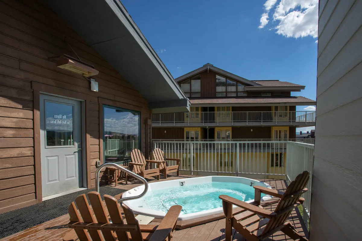 This image showcases an inviting outdoor jacuzzi area with wooden chairs, set against a backdrop of the building and surrounding alpine scenery. The setup suggests relaxation and socializing opportunities with views of the mountains.