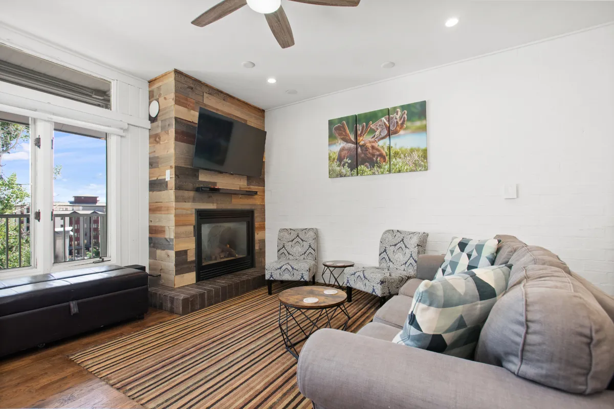 This image features a welcoming living area anchored by a barnwood-style fireplace, a plush sofa, modern artwork, and a sturdy coffee table. The setting is warm and inviting, perfect for gathering after a day on the slopes. The hardwood floors and stylish décor echo the modern mountain vibe described in the section.