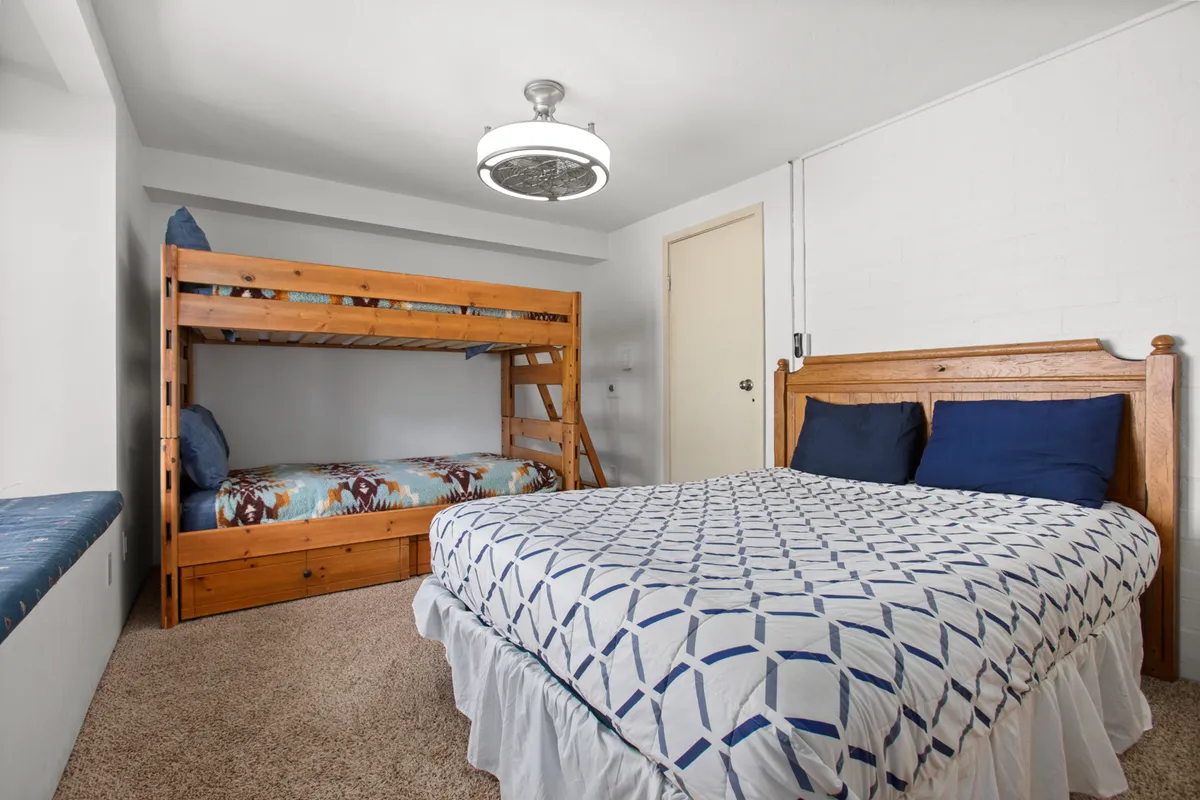This image features a welcoming bedroom with both a bunk bed and a double bed, accentuated by a decorative light fixture and a cozy window seat. The room is styled with playful yet comfortable touches, ideal for families, friends, or singles seeking flexibility and warmth.