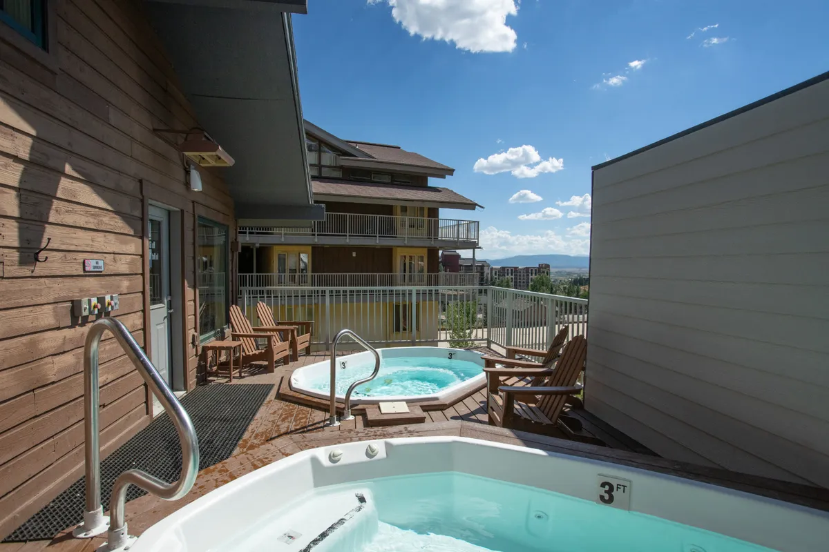 An inviting outdoor hot tub sits on a balcony surrounded by wooden chairs, with a view stretching to the mountains and sky. The scene is tranquil yet social, ideal for unwinding after a day on the slopes or gathering for evening chats under the stars.