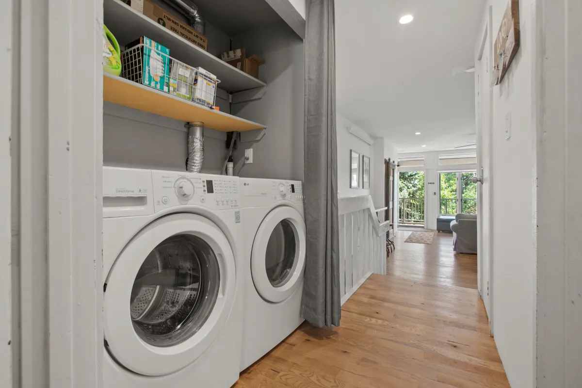 A practical laundry area is depicted with a washing machine, drying machine, and shelved storage. The scene is tidy and comfortable, reflecting convenience and the ease of extended stays.