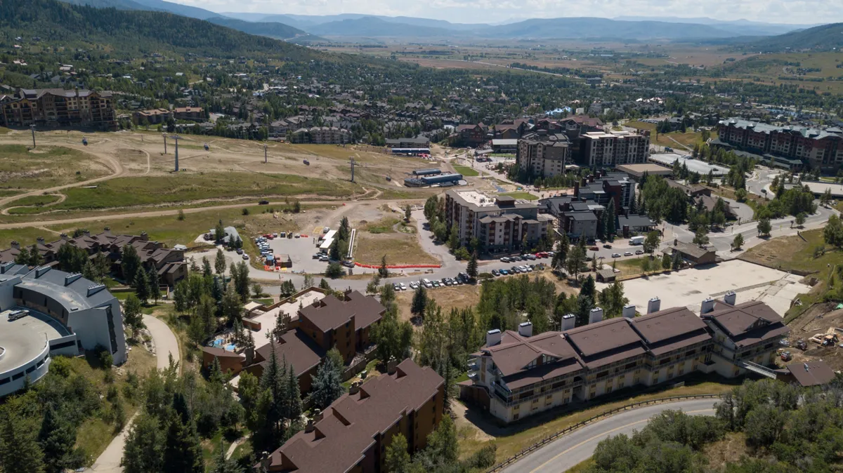 The image shows an energetic outdoor scene with residential buildings, green open spaces, and a mountain backdrop. Community gathering spots and accessible outdoor spaces suggest opportunities for family activities and social connection close to home.