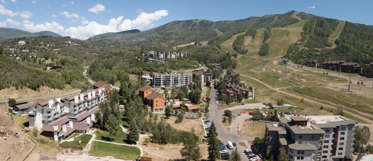 Looking out over lush green spaces, residential buildings, and distant mountain slopes, this image captures summertime trail access, hiking, biking, and the energetic atmosphere of Steamboat's base area during warmer months.